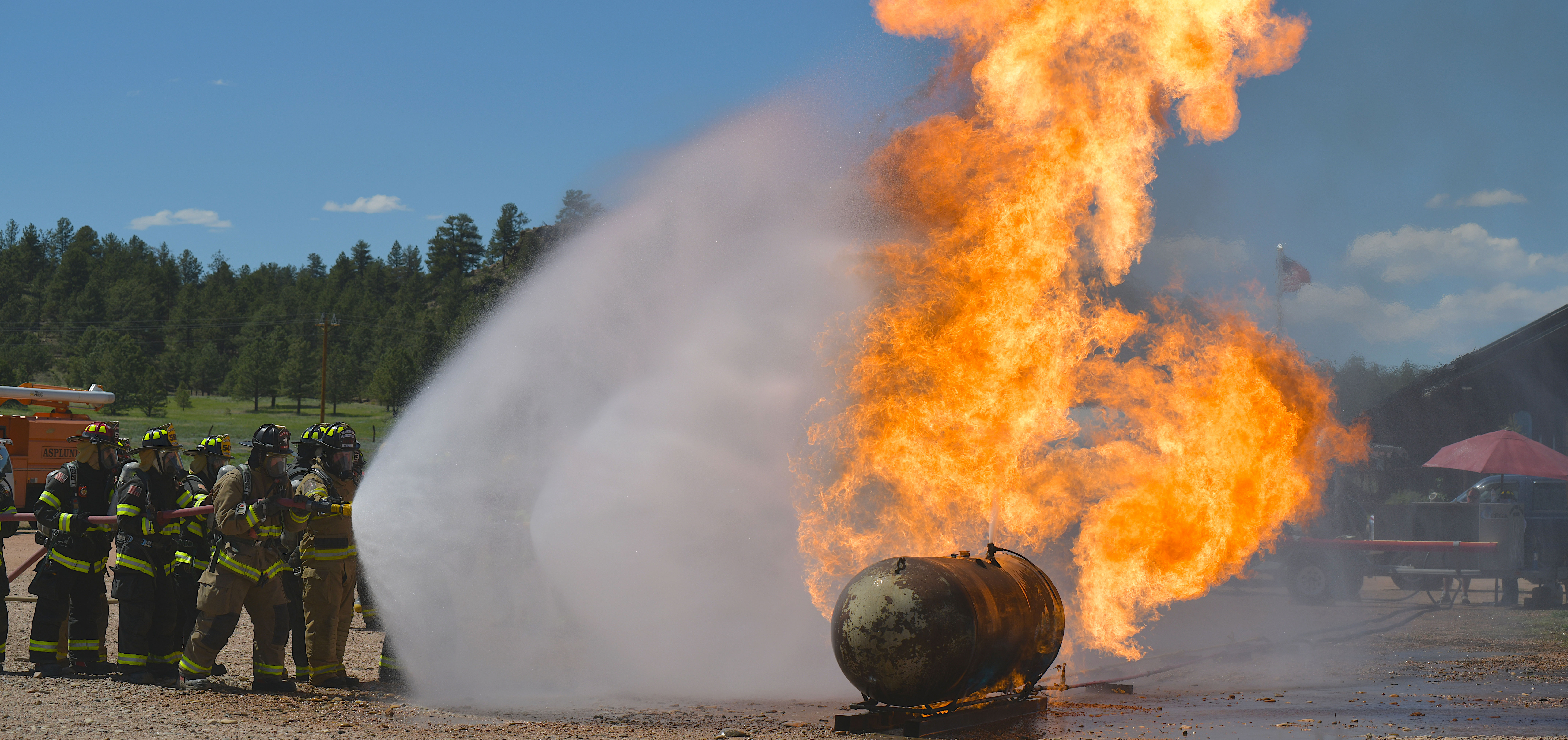 Fire fighters spraying water from a hose onto flames billowing from large propane tank